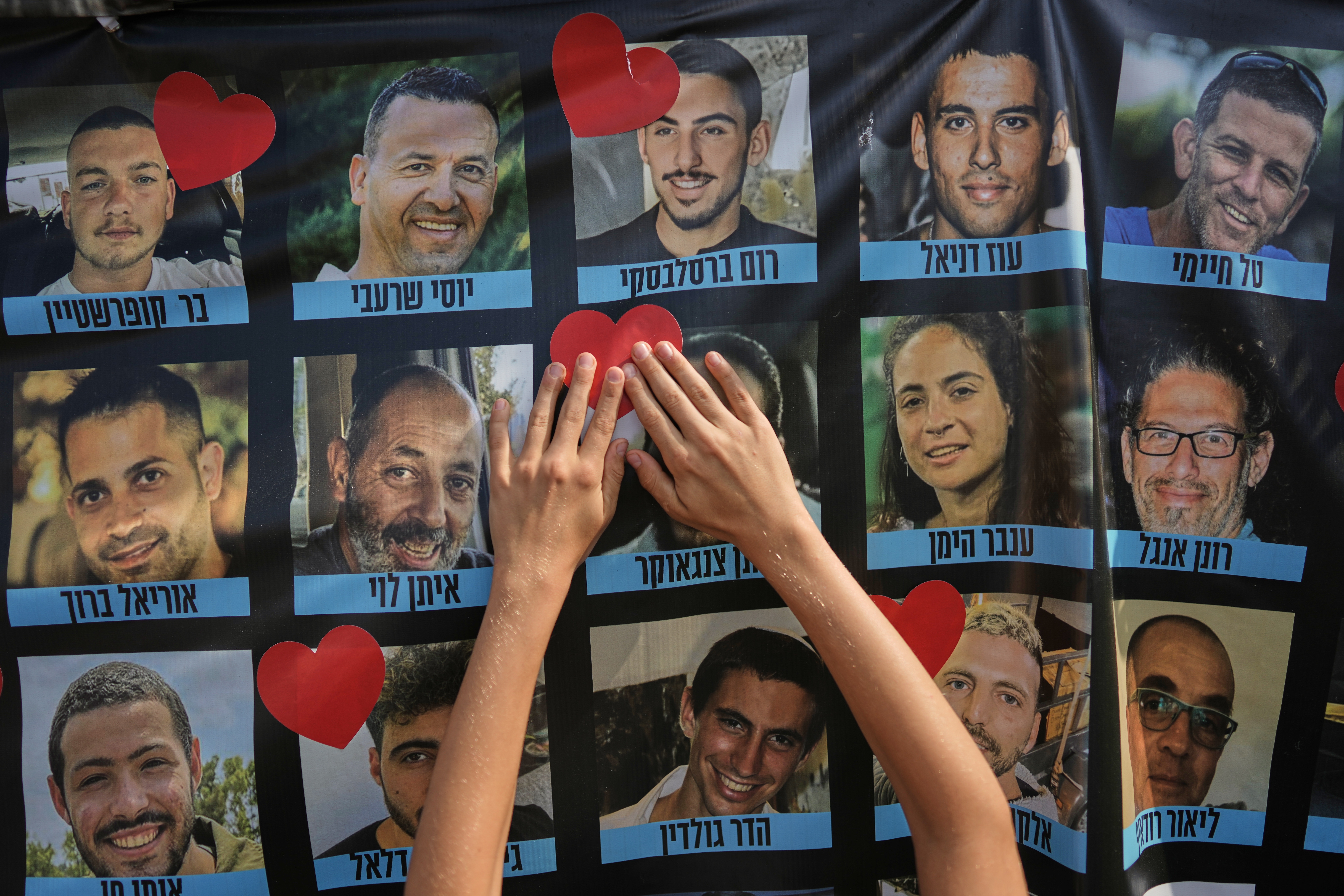 A person pastes a heart-shaped sticker on a banner with pictures of Israeli hostages during a a gathering at a plaza known as hostages square in Tel Aviv, Israel, Monday.